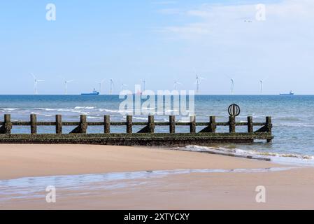 Offshore-Windpark vor der schottischen Küste an einem klaren Sommertag. Ein Groyne an einem Strand bei Ebbe steht im Vordergrund. Stockfoto