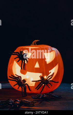 Geschnitzte Kürbis-Jack-o'-Laterne, beleuchtet von Kerzenlicht, Spinnen, schaffen eine gruselige Halloween-Atmosphäre Stockfoto