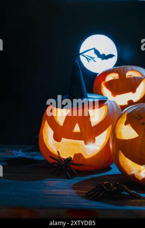 Drei leuchtende Jack-o'-Laternen in der Nacht bei Vollmond mit einer Fledermaus-Silhouette, die eine gruselige Halloween-Dekoration schaffen Stockfoto