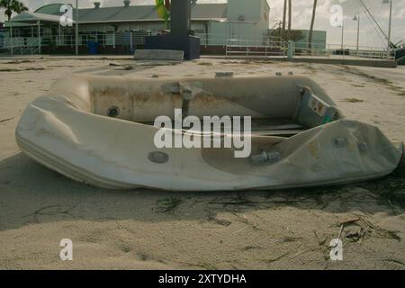 Ein kleines weißes Ruderboot lag nach einem großen Sturm am Ufer. Gulfport Florida mit dem Strand und dem blauen Himmel im Hintergrund. An einem sonnigen Tag. Stockfoto