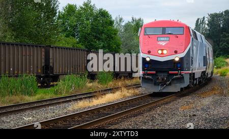 Everett, WA, USA - 28. Juli 2024; Amtrak Empire Builder Zug fährt mit einem Güterzug mit Scheinwerfern vorbei Stockfoto