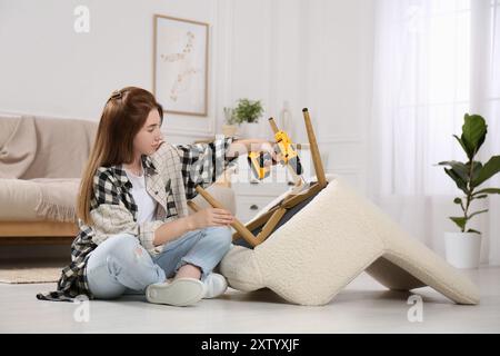 Frau mit elektrischem Schraubenzieher, der den Sessel zu Hause zusammenbaut Stockfoto