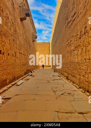 Ein Besucher bewundert die Basreliefs auf den aufwändig geschnitzten Sandsteinmauern im Tempel des Horus in Edfu, der während der ptolemäischen Ära zwischen 237 und 57 v. Chr. in der Nähe von Assuan, Ägypten, erbaut wurde Stockfoto