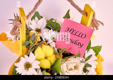 Die Worte HALLO DIENSTAG auf einem Aufkleber in einem Korb mit Blumen Stockfoto