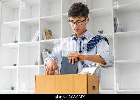 Trauriger junger Geschäftsmann, der seine Sachen in eine Kiste packt, bevor er sein Büro nach seinem Rücktritt verlässt Stockfoto