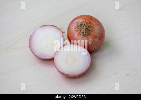 Eine ganze Zwiebel und eine in zwei Stücke geschnittene Zwiebel auf hölzernem Hintergrund. Stockfoto