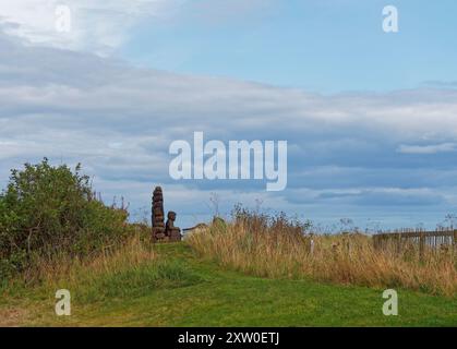 Eine Holzskulptur eines Fischers, der seine Netze pflegt, während er auf das Meer blickt, im kleinen Fischerdorf East Haven in der Nähe von Arbroath. Stockfoto