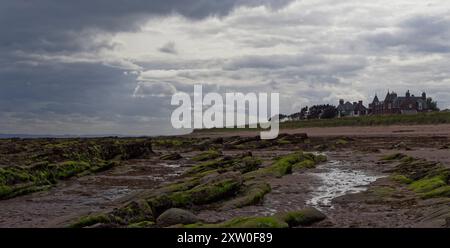 Große alte traditionelle Häuser mit Blick auf den Strand bei Ebbe in dem kleinen Dorf East Haven mit dunklen Regenwolken, die über dem Meer heraustreten. Stockfoto