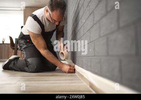 Der Mann klebt Schutzband an die Wand, bevor er lackiert Stockfoto