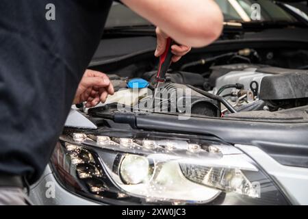 Ein erfahrener Techniker überprüft den Motorraum eines modernen Fahrzeugs sorgfältig. Mit einem Schraubendreher arbeitet der Mechaniker an wichtigen Bauteilen Stockfoto