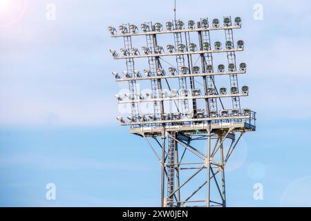 Eine hoch aufragende Sportfluter-Struktur, ausgestattet mit mehreren hellen Lichtern, beleuchtet den Bereich für Abendveranstaltungen. Der klare blaue Hintergrund enhan Stockfoto