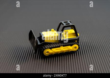 Gelbes Miniatur-Bulldozer-Spielzeug auf schwarzem Hintergrund Stockfoto