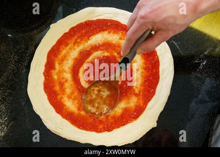 Ansicht von oben nach unten: Tomatensauce auf Pizzateig mit einem Löffel Stockfoto