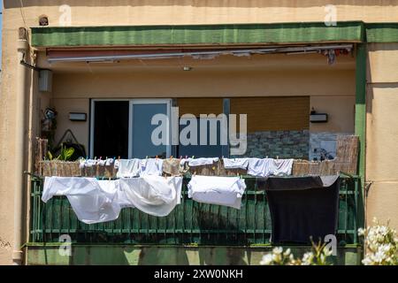 Kleidung und Bettwäsche hängen zum Trocknen auf dem Balkon eines Appartementgebäudes und klingen im hellen Sonnenlicht. Stockfoto