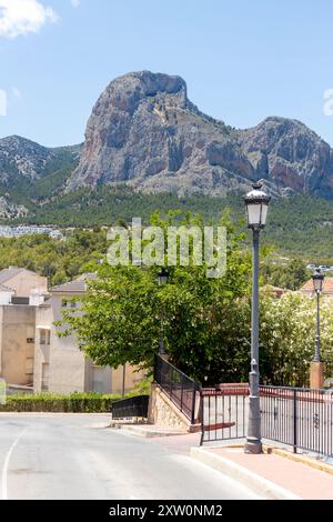 Eine ruhige Straße in einem Dorf mit Blick auf einen hohen felsigen Berg im Hintergrund, umgeben von Grün. Stockfoto