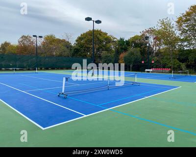 Tragbare Pickleball-Netze, die auf zwei blauen und grünen Tennisplätzen platziert werden, um vier Pickleball-Plätze mit Lichtern zu machen, um nachts spielen zu können. Stockfoto
