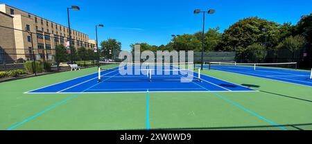 Vorderansicht der tragbaren Pickleball-Netze, die auf zwei blauen und grünen Tennisplätzen platziert werden, um vier Pickleball-Plätze mit Lichtern zu machen, um am Nig spielen zu können Stockfoto