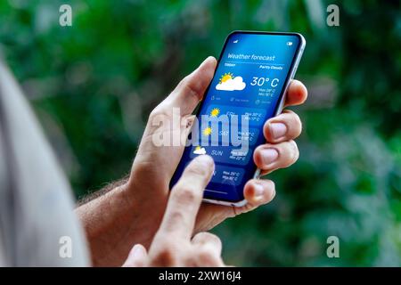 Mann draußen, der Wettervorhersage auf seinem Handy überprüft. Stockfoto