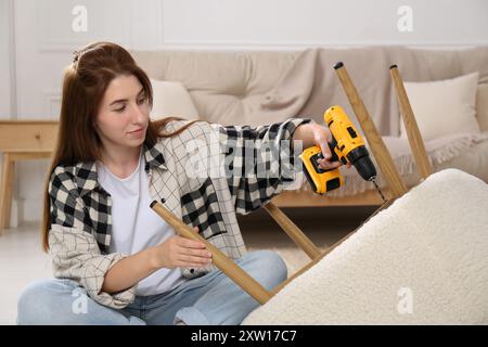 Frau mit elektrischem Schraubenzieher, der den Sessel zu Hause zusammenbaut Stockfoto