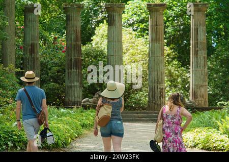 Drei Touristen erkunden die Ruinen der dorischen Steinsäule in R.H.S. Gardens, Harlow Carr, Harrogate, Yorkshire, Großbritannien, umgeben von Grün. Stockfoto