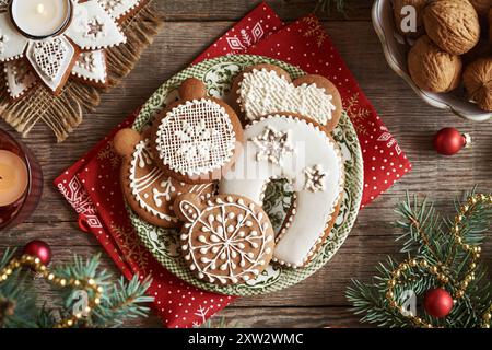 Hausgemachte Lebkuchen Weihnachtskekse mit weißer Glasur auf grünem Teller mit Fichtenzweigen, Walnüssen und Kerzen, Blick von oben Stockfoto