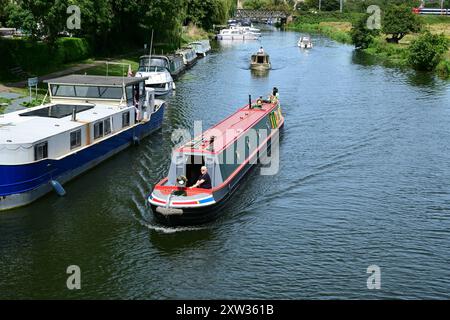 Schmales Boot, das an festgefahrenen Schiffen auf dem Fluss Great Ouse, Ely, Cambridgeshire, England, Großbritannien vorbeifährt Stockfoto
