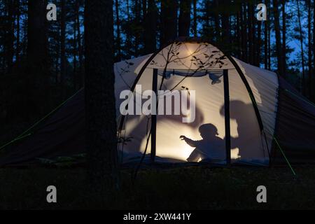 Silhouetten von Kindern, die nachts im Campingzelt spielen und während der Sommerferien Schattenpuppen mit Taschenlampe machen Stockfoto