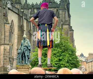 Edinburgh, Schottland, Großbritannien. August 2024. Wetter in Großbritannien: ein Darsteller in einem zeitgenössischen Kilt spiegelt die adam smith Statue auf der Royal Mile feuchtes Wetter wich einer angenehmen Royal Mile und einem Hügel, der große Menschenmengen von Einheimischen und Touristen in der Stadt sah, während Künstler die Initiierung durchmachten, Flugblätter für ihre Shows zu verteilen. Credit Gerard Ferry/Alamy Live News Stockfoto