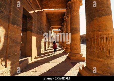 Ein Besucher spaziert durch die wunderschönen Kollonaden im Innenhof in der goldenen Abendsonne am Tempel der Isis auf Philae Island am Nasser-See, erbaut von Nectanebo und Ptolemaios Pharoahs in der Nähe von Assuan, Ägypten Stockfoto