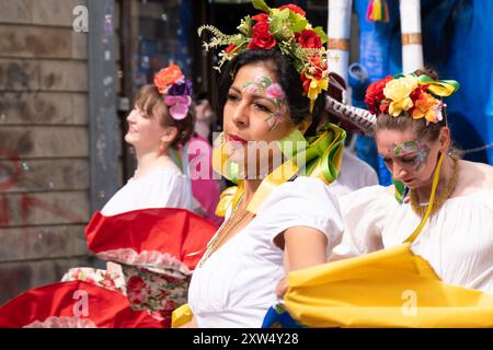 Belfast Mela Karnevalsparade - schöne Frauen mit Blumengemälden auf dem Gesicht in exquisitem, farbenfrohen Kostüm. Belfast, Großbritannien - 17. August 2024. Stockfoto