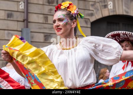 Belfast Mela Karnevalsparade - Blumenmuster der Frau im Gesicht mit bunten Blumen im Haar, die ein auffälliges Kostüm tragen. Belfast, Großbritannien - 17. August 2024. Stockfoto