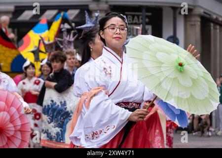 Belfast Mela Karnevalsparade - elegante Dame in traditioneller japanischer Tracht mit grünem Sonnenschirm bewegt sich mit großer Pose. Belfast, Großbritannien - 17. August 2024. Stockfoto