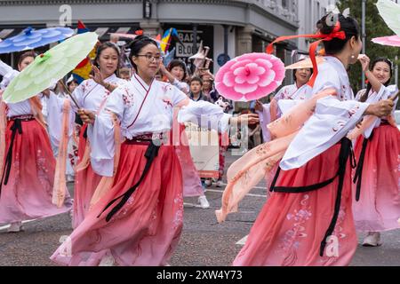 Belfast Mela kulturelle Karnevalsparade - Gruppe von Damen in traditioneller japanischer Tracht mit bunten Sonnenschirmen, die tanzen. Belfast, Großbritannien - 17. August 2024. Stockfoto