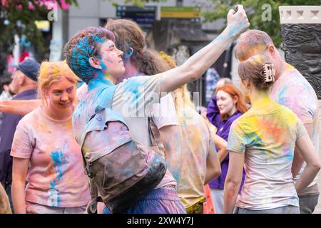 Jährlicher Belfast Mela Karneval - eine Gruppe junger Männer und Frauen, die mit lebhaftem, farbenfrohem Gulalpulver bedeckt sind. Belfast, Großbritannien - 17. August 2024. Stockfoto