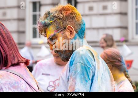 Jährliche Belfast Mela Carnival Parade - junger Mann mit Bart und Brille, bedeckt mit farbenfrohen Gulal Pulver. Belfast, Großbritannien - 17. August 2024. Stockfoto