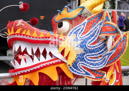 Jährliche Belfast Mela Carnival Parade - Nahaufnahme des Kopfes des chinesischen tanzenden Drachen in auffälligen Rot- und Orangenfarben. Belfast, Großbritannien - 17. August 2024. Stockfoto