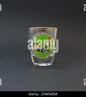 Ein Vintage-Shot-Glas, das als Souvenir an die FIFA Fußball-Weltmeisterschaft im Juni-Juli 1974 in der Bundesrepublik Deutschland hergestellt wurde. Das Glas ist mit dem komischen Cartoonbild der offiziellen Turniermaskottchen „Tip“ & „Tap“ verziert, umgeben von der Überschrift „Fussball-Weltmeisterschaft 1974 – in der Bundesrepublik Deutschland“ (Fußball-Weltmeisterschaft 1974 – in der Bundesrepublik Deutschland). Die FIFA Fussball-Weltmeisterschaft 1974 fand vom 13. Juni bis 7. Juli in der Bundesrepublik Deutschland statt. Dieses Turnier war das erste Mal, dass die aktuelle Trophäe, die FIFA Fussball-Weltmeisterschaft, verliehen wurde. Stockfoto