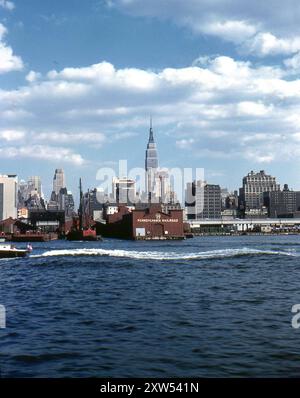 New York, USA. September 1959: Ein Blick auf den Pier 77, den Güterpier der Pennsylvania Railroad, vom Hudson River aus, New York. In der Ferne sind das New Yorker Hotel und das Empire State Building zu sehen. Ein großes Werbeschild befindet sich im Gebäude der Hobb Electrical Supply Corp, das sich an der 34th und 35th Street befindet. Stockfoto