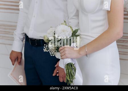 Eleganter Hochzeitsmoment mit Braut und Bräutigam, die Hände und einen Blumenstrauß halten und Liebe und Einheit symbolisieren Stockfoto
