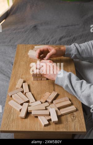 Person, die Holzblöcke stapelt, Turm baut, während sie an einem Tisch im Freien sitzt, konzentriert sich auf das Ausbalancieren der Teile. Nahaufnahme Stockfoto