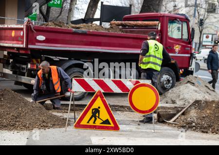 en bei der Arbeit, in Schutzkleidung gekleidet, schwere Maschinen bedienen, während ein Arbeiter einen Graben aushebt, um Sicherheit und Teamarbeit auf der Baustelle zu gewährleisten Stockfoto