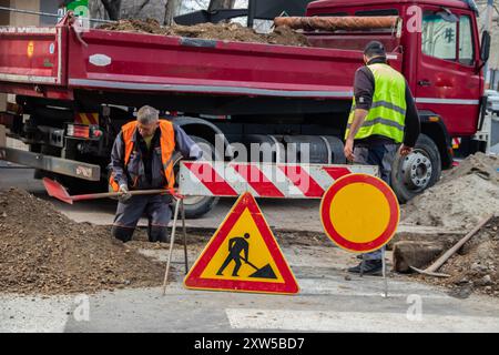 en bei der Arbeit, in Schutzkleidung gekleidet, schwere Maschinen bedienen, während ein Arbeiter einen Graben aushebt, um Sicherheit und Teamarbeit auf der Baustelle zu gewährleisten Stockfoto