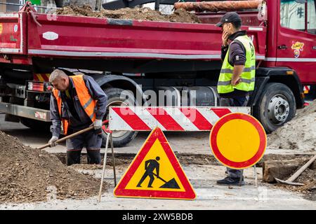 en bei der Arbeit, in Schutzkleidung gekleidet, schwere Maschinen bedienen, während ein Arbeiter einen Graben aushebt, um Sicherheit und Teamarbeit auf der Baustelle zu gewährleisten Stockfoto