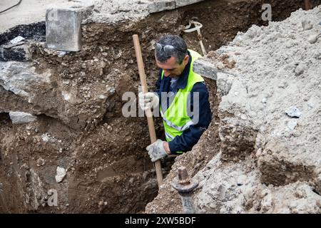 en bei der Arbeit, in Schutzkleidung gekleidet, schwere Maschinen bedienen, während ein Arbeiter einen Graben aushebt, um Sicherheit und Teamarbeit auf der Baustelle zu gewährleisten Stockfoto