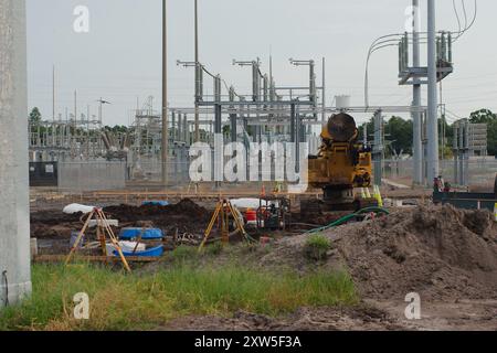 Weitsicht-Schotterhaufen links zur elektrischen Umspannstation für Baumaschinen mit Hochspannungsleitungen in St. Petersburg, Florida. Blick auf das grüne Gras Stockfoto