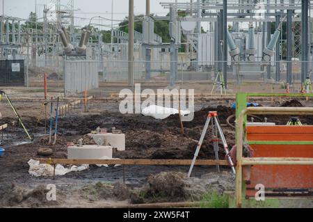 Weitsicht-Schotterhaufen links zur elektrischen Umspannstation für Baumaschinen mit Hochspannungsleitungen in St. Petersburg, Florida. Blick auf das grüne Gras Stockfoto