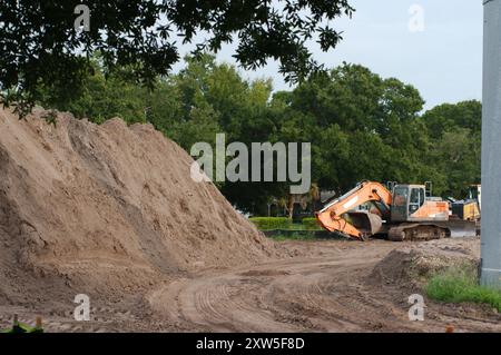 Weitsicht-Schotterhaufen links zur elektrischen Umspannstation für Baumaschinen mit Hochspannungsleitungen in St. Petersburg, Florida. Blick auf das grüne Gras Stockfoto