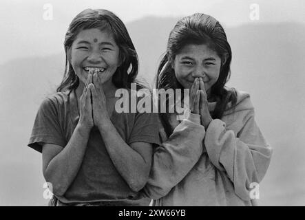 Zwei lachende Schwestern grüßen den Namaste in den mittleren Hügeln Nepals auf dem Annapurna Sanctuary Trek - Nepal 1988 Stockfoto