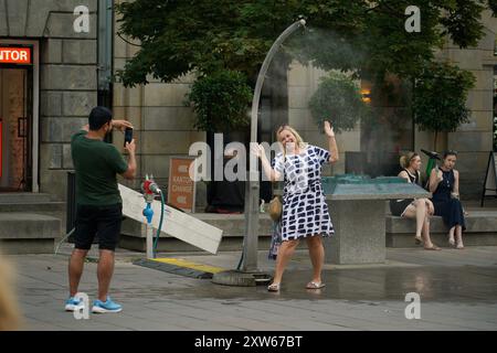 Warschau, Polen. August 2024. Eine Frau posiert am 17. August 2024 in Warschau, Polen, für ein Foto mit einem Nebelkühlsystem. Quelle: Jaap Arriens/Xinhua/Alamy Live News Stockfoto