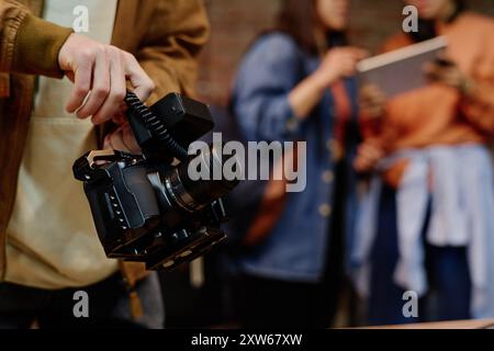 Person, die eine professionelle Kamera hält und mit Freunden in Studioumgebung mit verschwommenem Hintergrund fotografiert Stockfoto